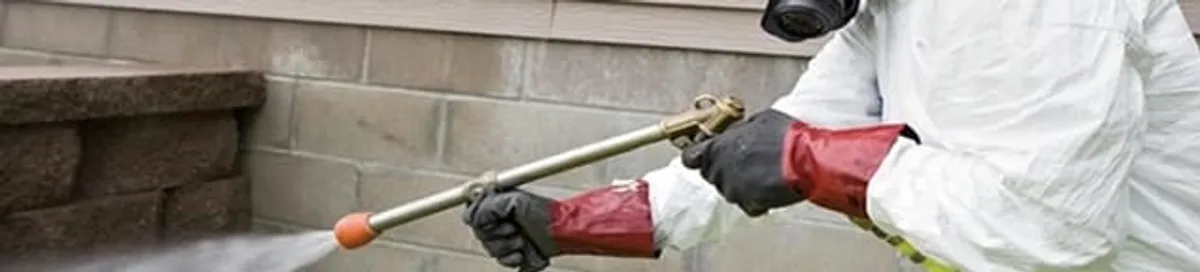 Pest control technician applying exterior insect treatment along a home foundation in Honolulu, HI