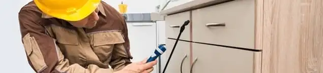 Roach exterminator applying treatment under kitchen cabinets in Honolulu, HI
