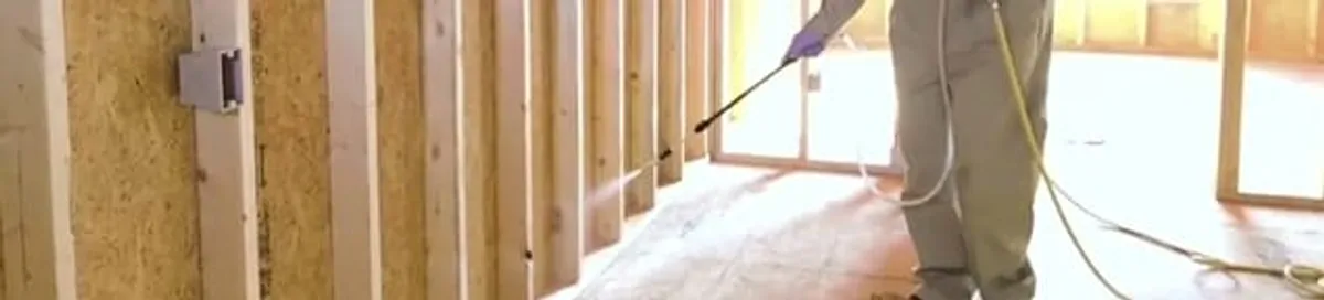 Termite treatment technician applying spray along framing and unfinished walls in Honolulu, HI