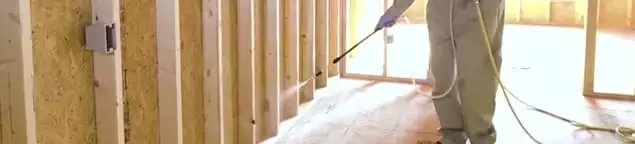 Termite treatment technician applying spray along framing and unfinished walls in Honolulu, HI